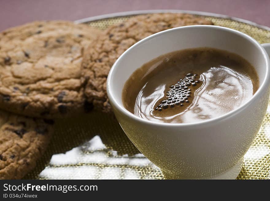 Coffee cup and chocolate cookies on a plate over color background