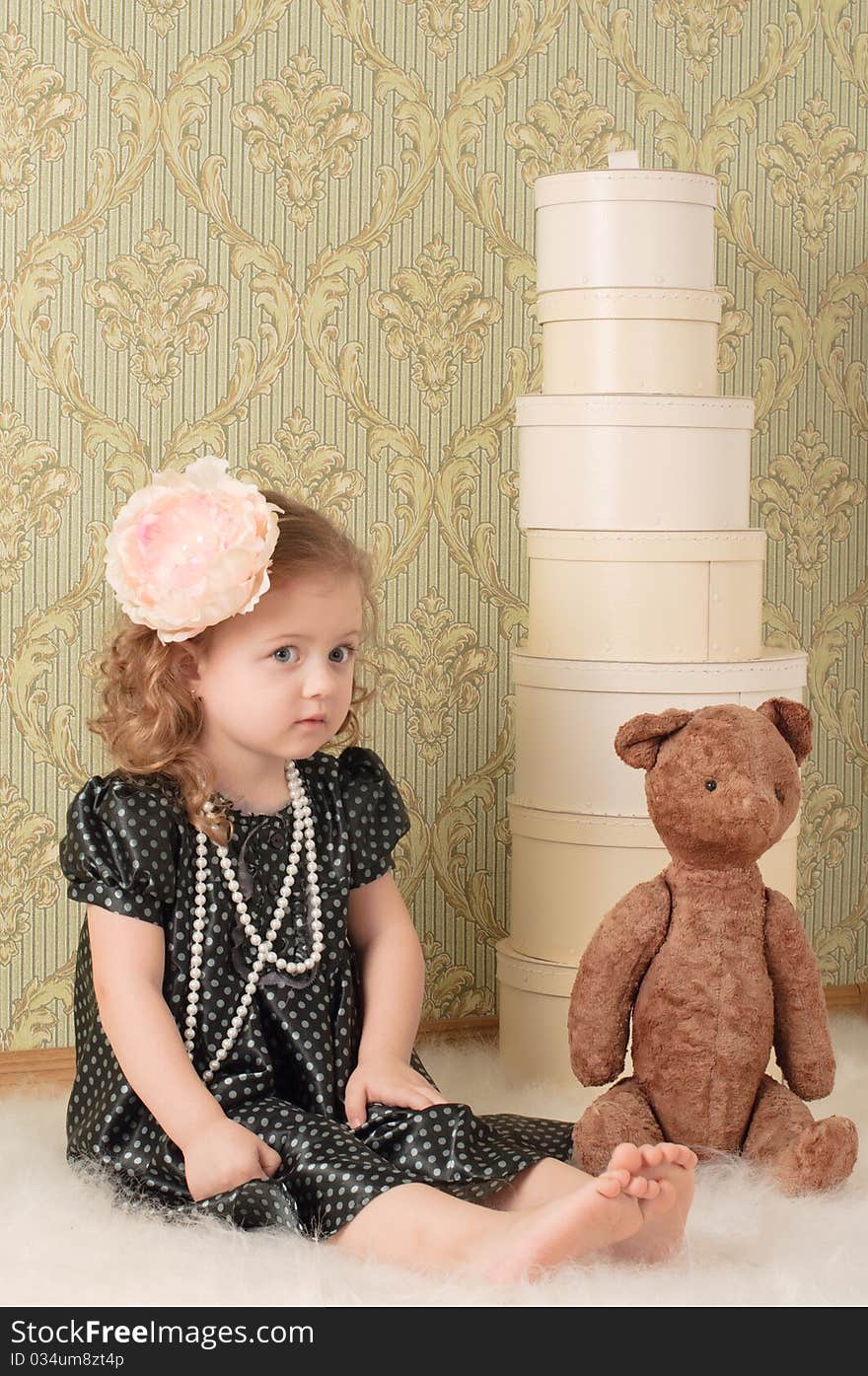 Little girl dressed as a retro doll sits on the floor with a toy