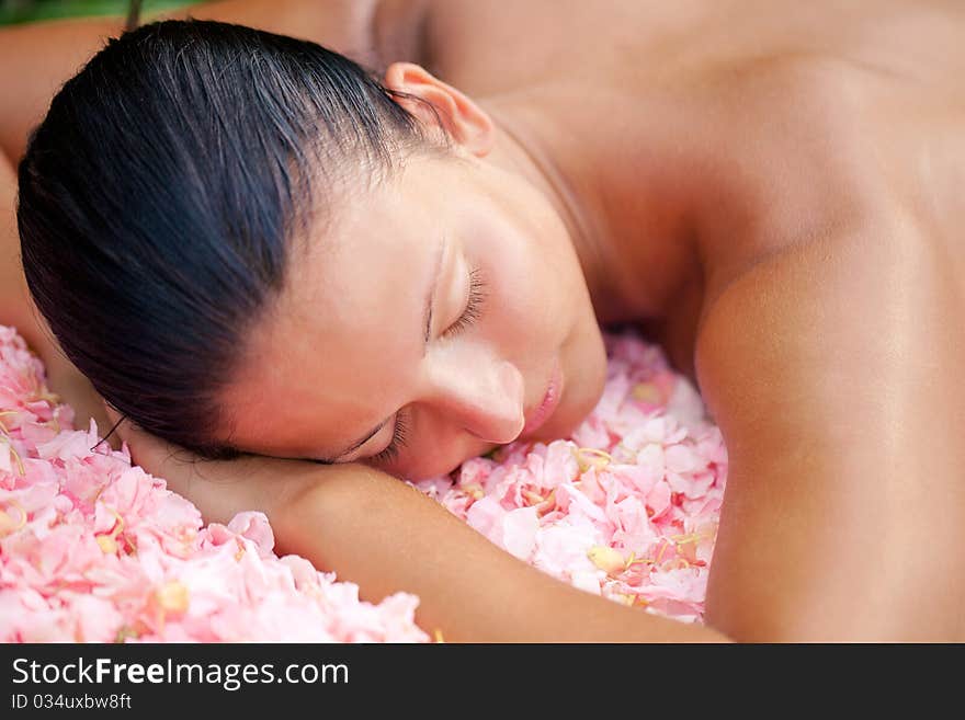 Beautiful woman relaxing on the massage table covered by flowers