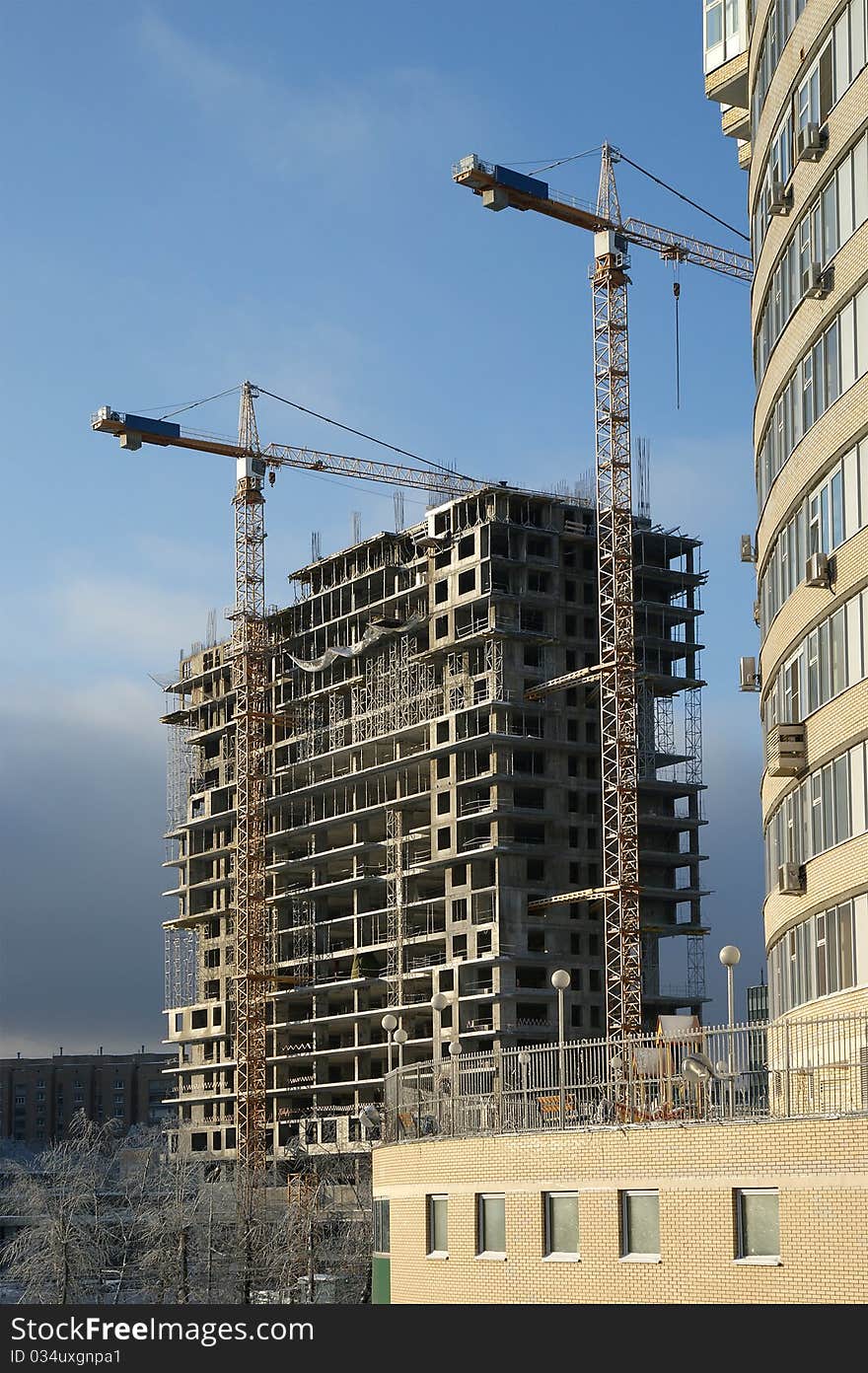 Elevating construction crane and building under construction on the blue clear sky