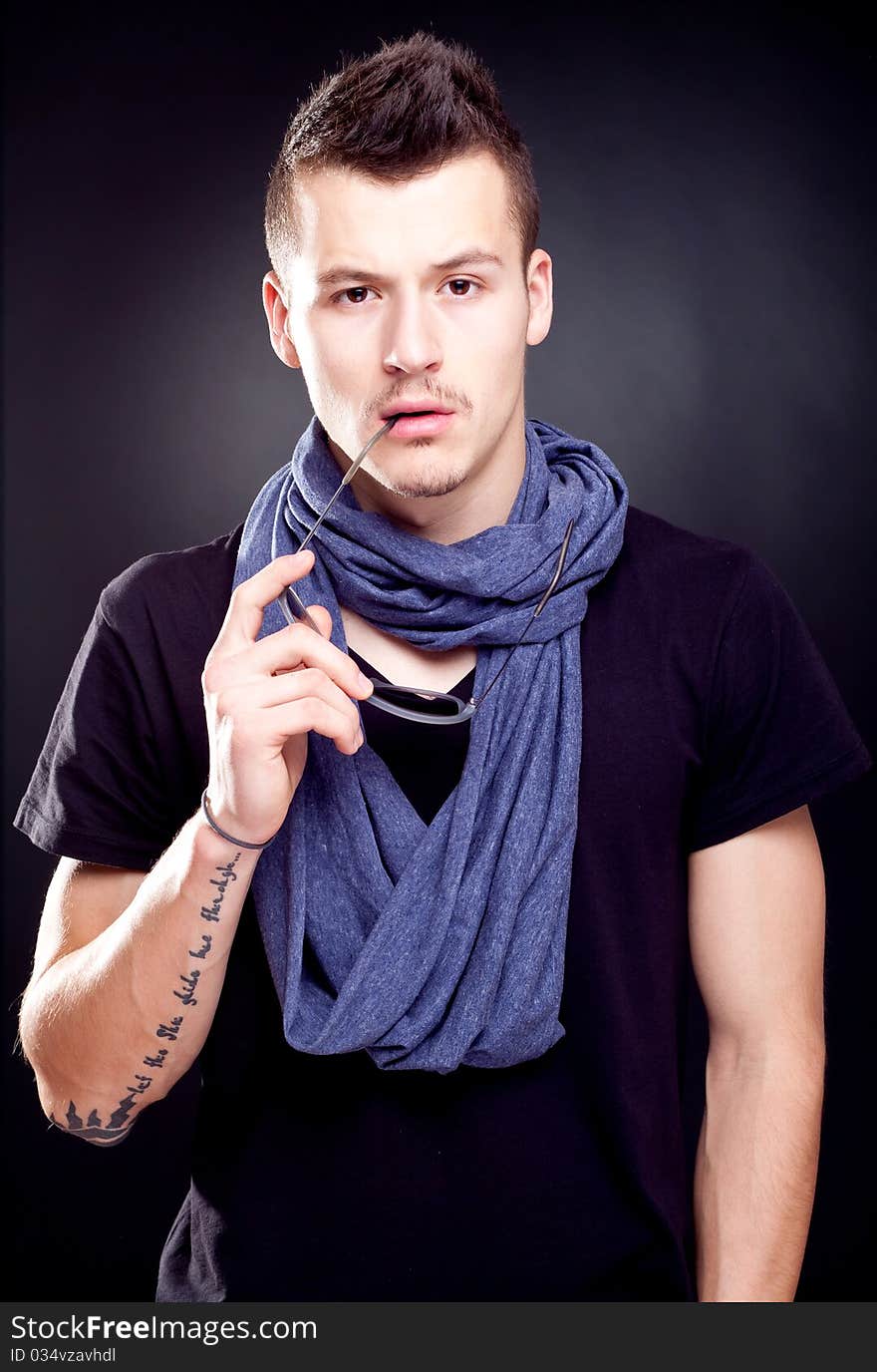 Studio shot of a handsome young male model wearing T-shirt and holding sunglasses in his mouth