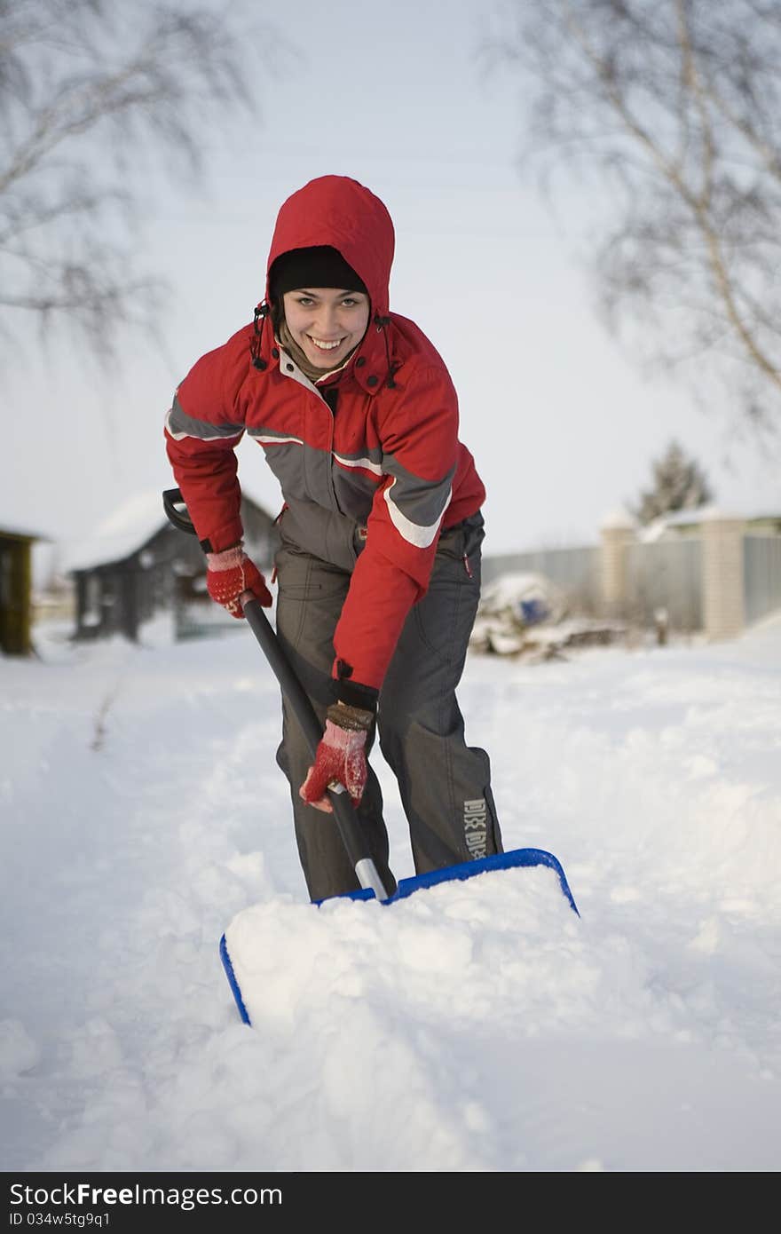 The girl in a red jacket and a hood cleans snow a