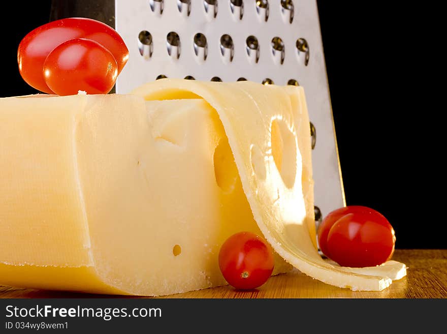 Swiss cheese slice, grater and red tomato on a wood desk.