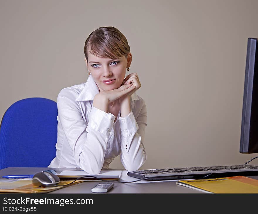 A young girl in the office sitting at the table, hands clasped and smiling