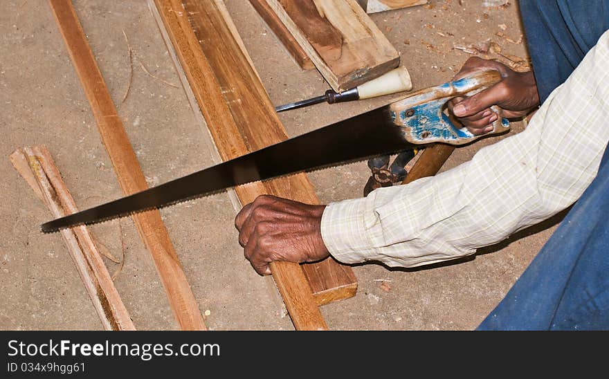 A carpenter using a hand saw for cutting wood. A carpenter using a hand saw for cutting wood.