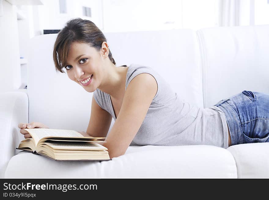 Young woman reading book in home interior on divan;