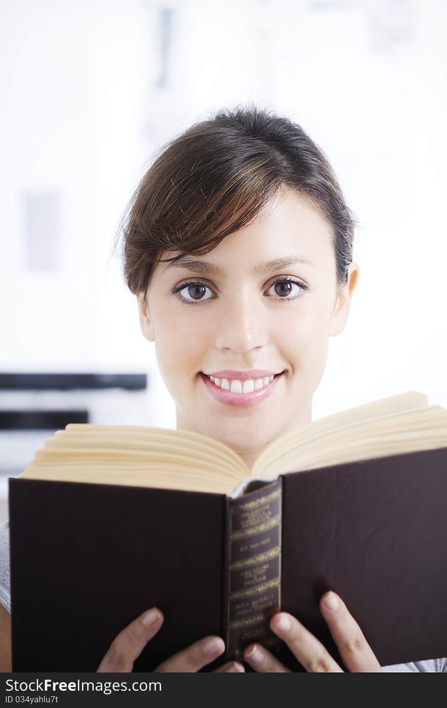 Woman reading book in home interior, smiling and looking in camera; concept of relax and entertainment. Woman reading book in home interior, smiling and looking in camera; concept of relax and entertainment