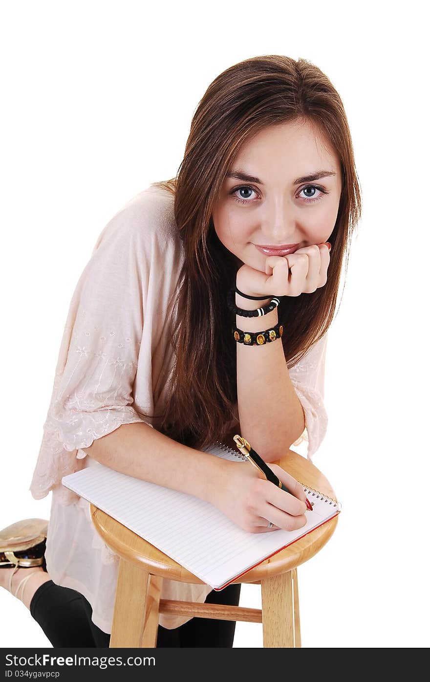 A beautiful teenager kneeling for a chair and writing in her notebook, smiling into the camera, for white background. A beautiful teenager kneeling for a chair and writing in her notebook, smiling into the camera, for white background.