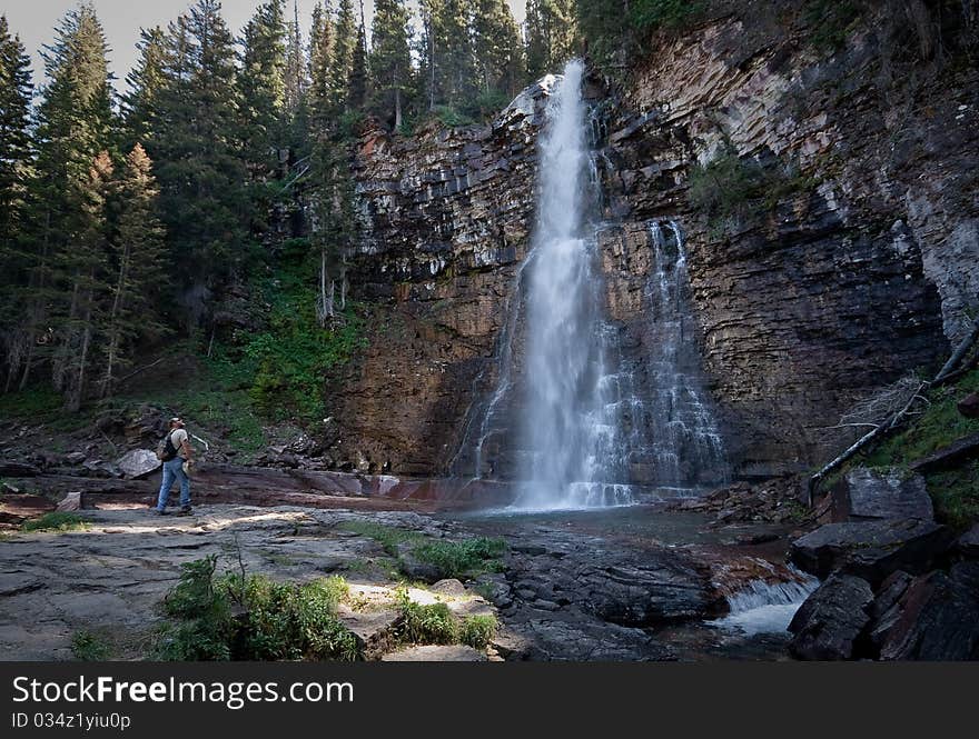 A man looks up at a waterfall in Glacier National Park.