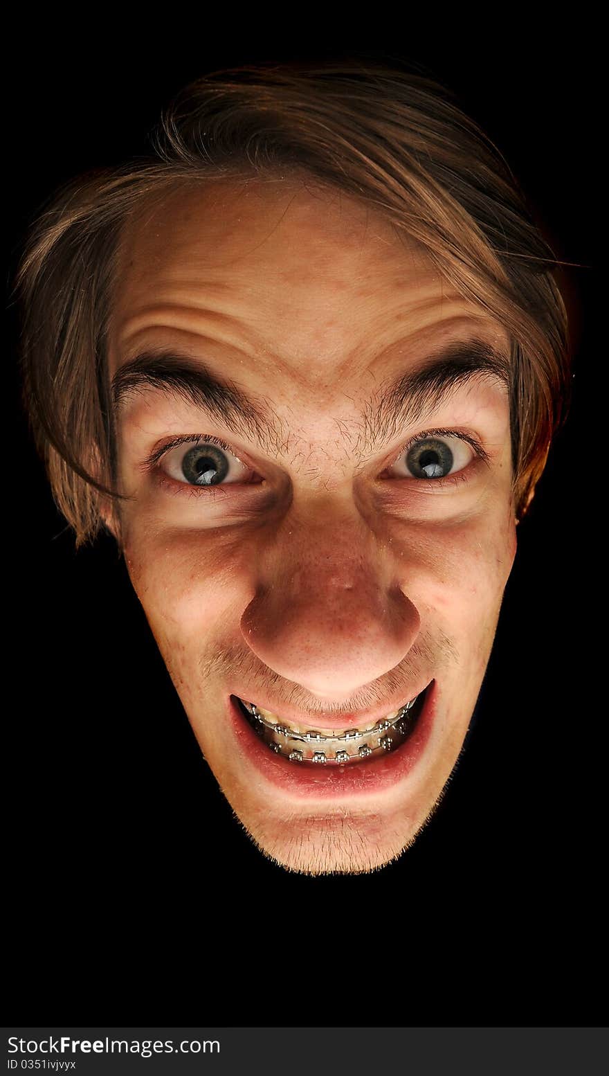 This man is clearly insane. Isolated head on black background. He is wearing braces with a big grin on this face, could be considored a mad scientist.