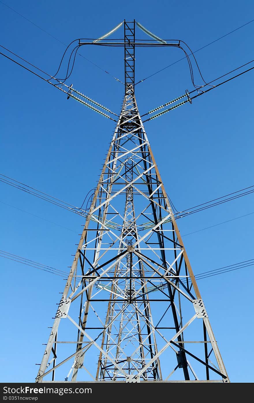 Power lines and electric pylon against a blue clear sky.