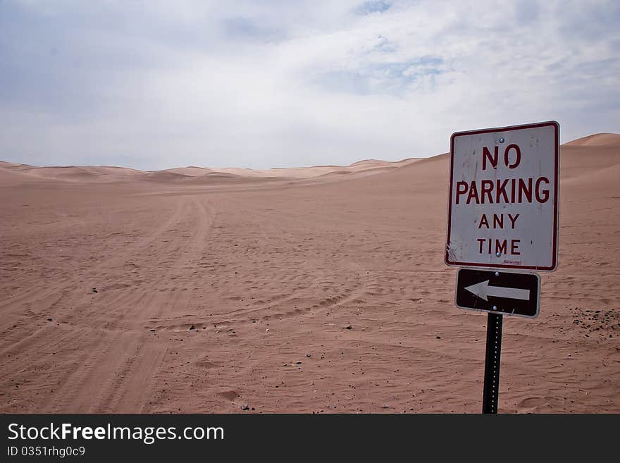 No parking any time traffic sign with arrow pointing to sand desert