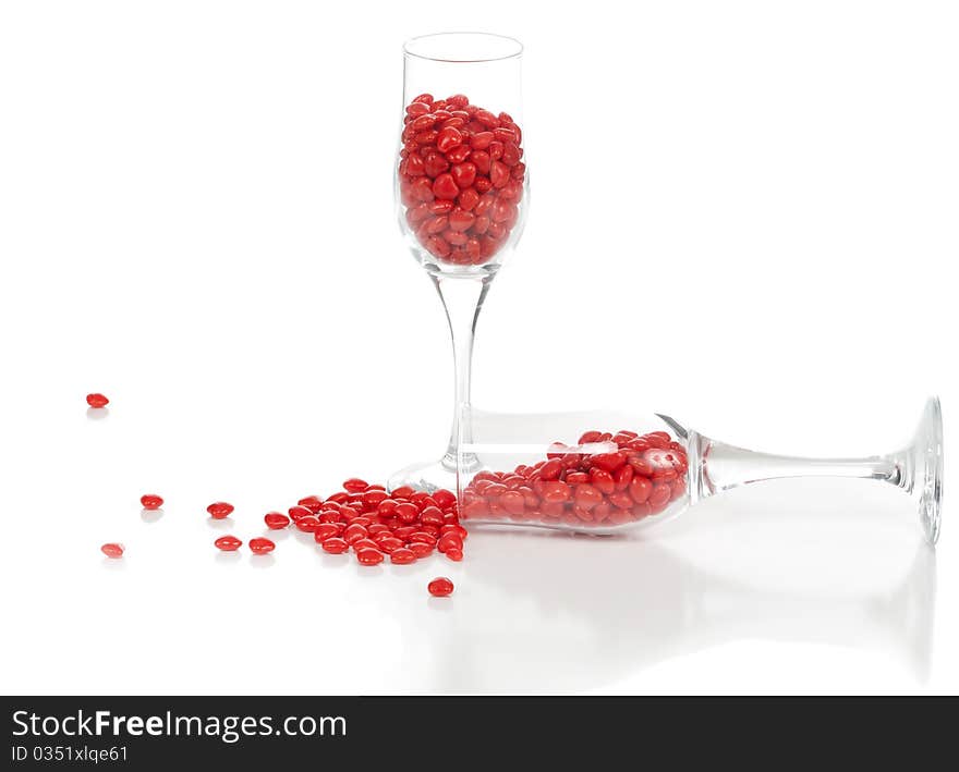 A front isolated studio view of cinnamon hearts spilled out of one of the two champagne glasses. A front isolated studio view of cinnamon hearts spilled out of one of the two champagne glasses.