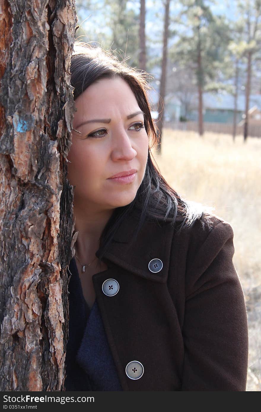 Beautiful brunette female leaning against a tree looking out. Beautiful brunette female leaning against a tree looking out