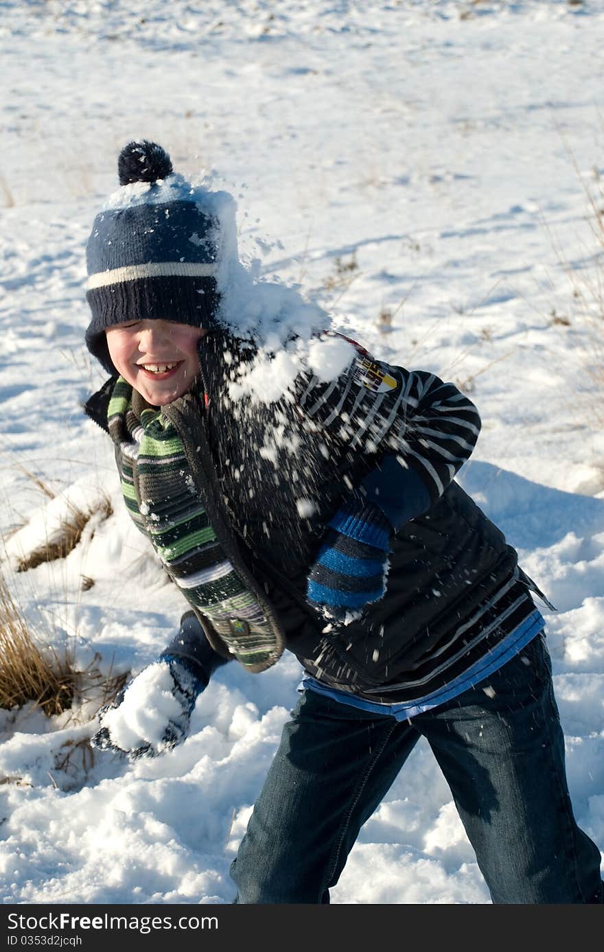 Little boy with blue winter hat having fun, throwing a snowball while getting a snowball against his head. Little boy with blue winter hat having fun, throwing a snowball while getting a snowball against his head