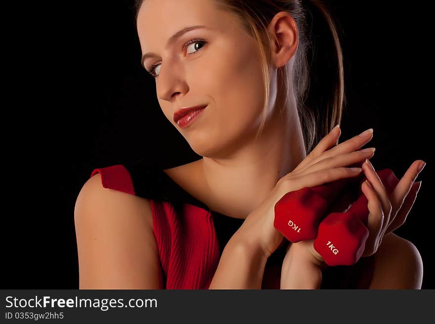 Young beautiful woman playing with two dumbbells on black background. Young beautiful woman playing with two dumbbells on black background