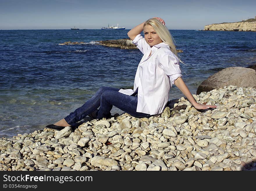 Blonde touching hair in white shirt and jeans near the sea with ships on horizon. Blonde touching hair in white shirt and jeans near the sea with ships on horizon