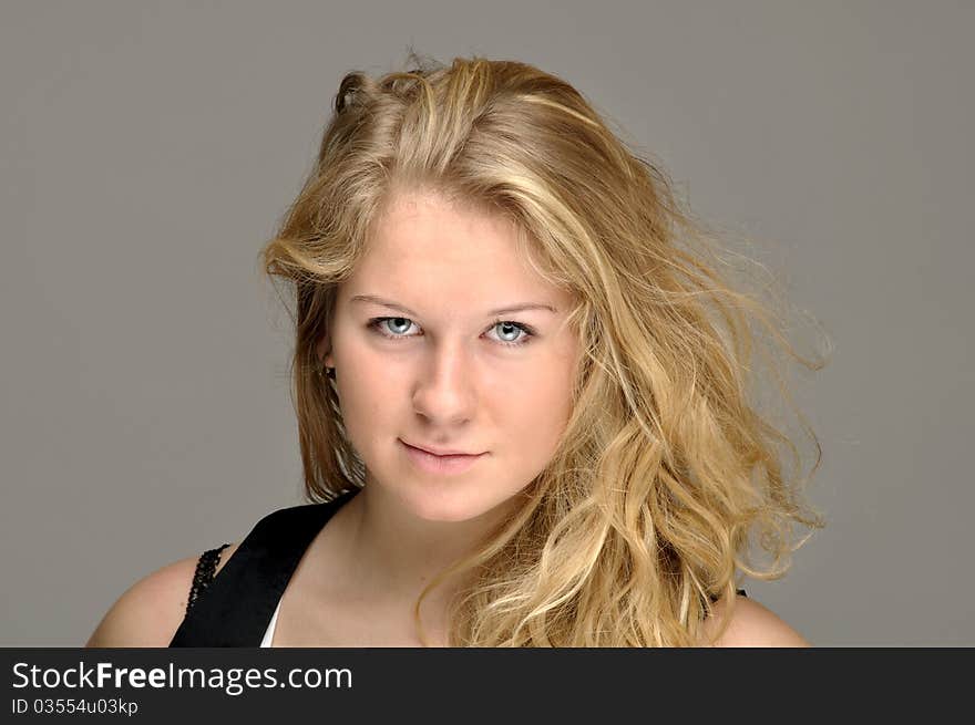 Young blond close-up against gray background. Hair is slightly tousled. Young blond close-up against gray background. Hair is slightly tousled