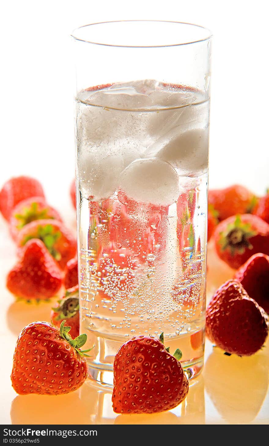 A glass of sparkling water and ice on a white background and strawberries