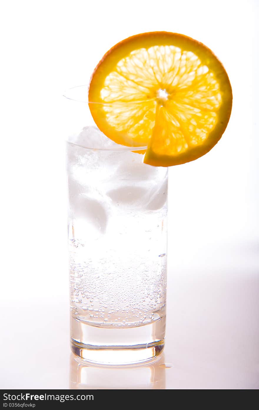 Isolated glass of soda with ice cold water on a white background with orange slice