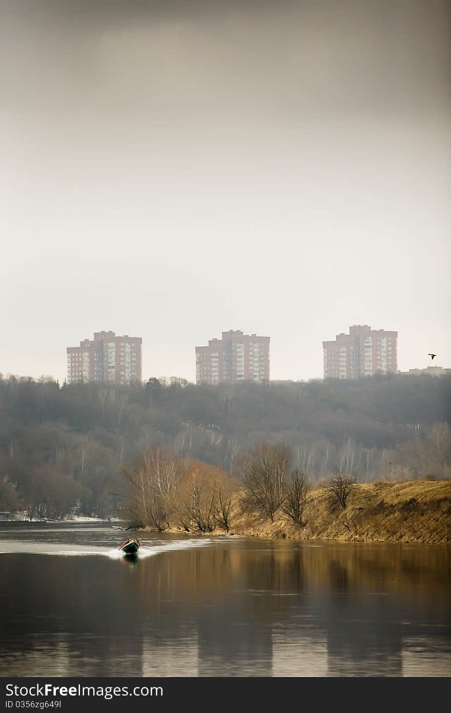 Spring landscape with a flowing river, a distant shore and the trees in bad weather