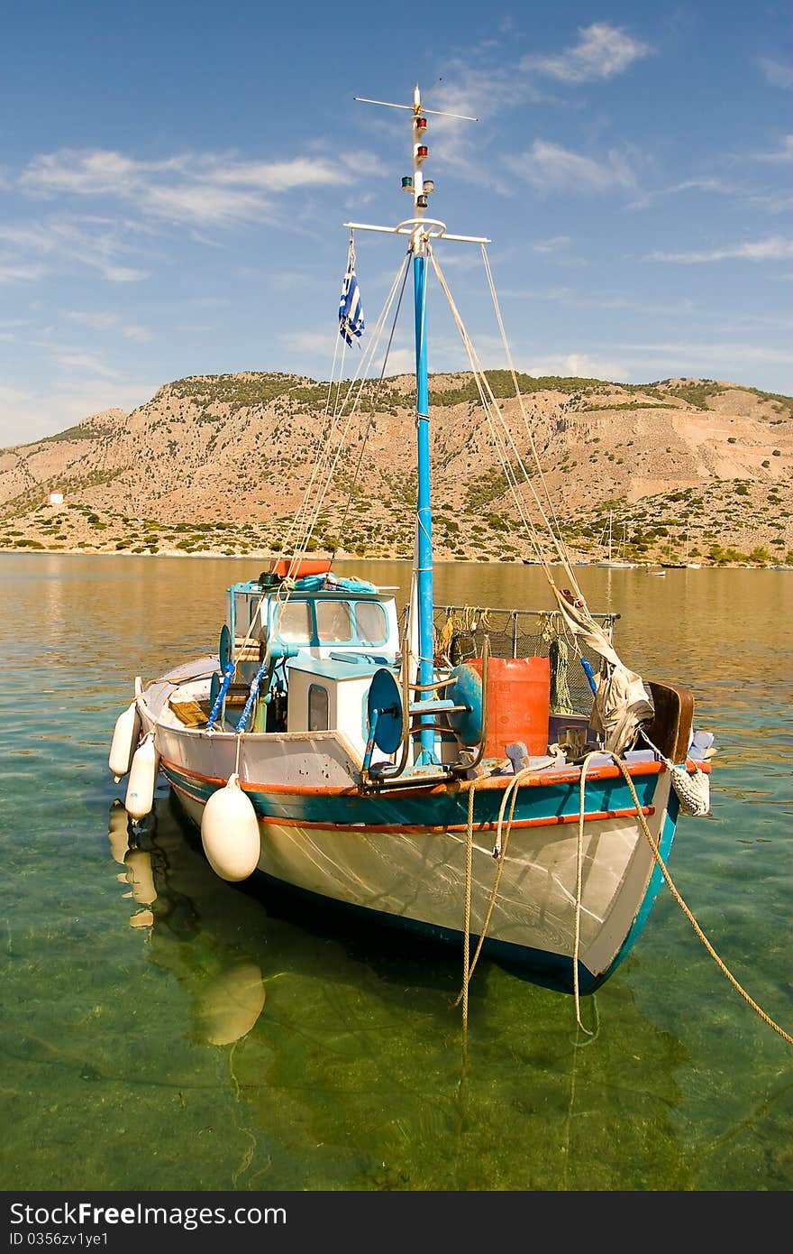 A small white fishing boat standing at a pier in a Mediterranean bay surrounded by mountains