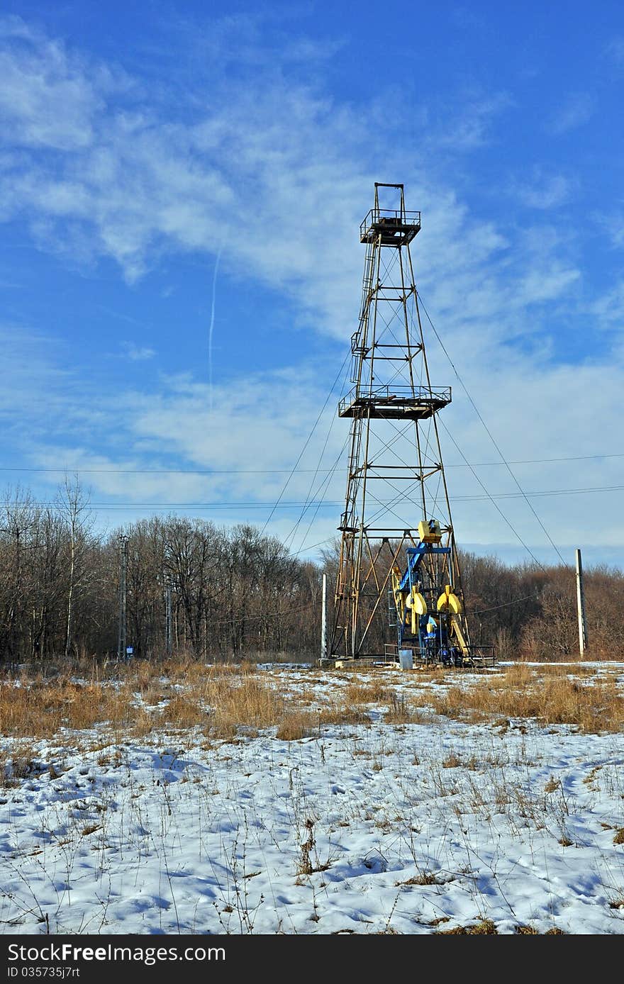 Oil probe working on snowy field near forest in a sunny winter day. Oil probe working on snowy field near forest in a sunny winter day