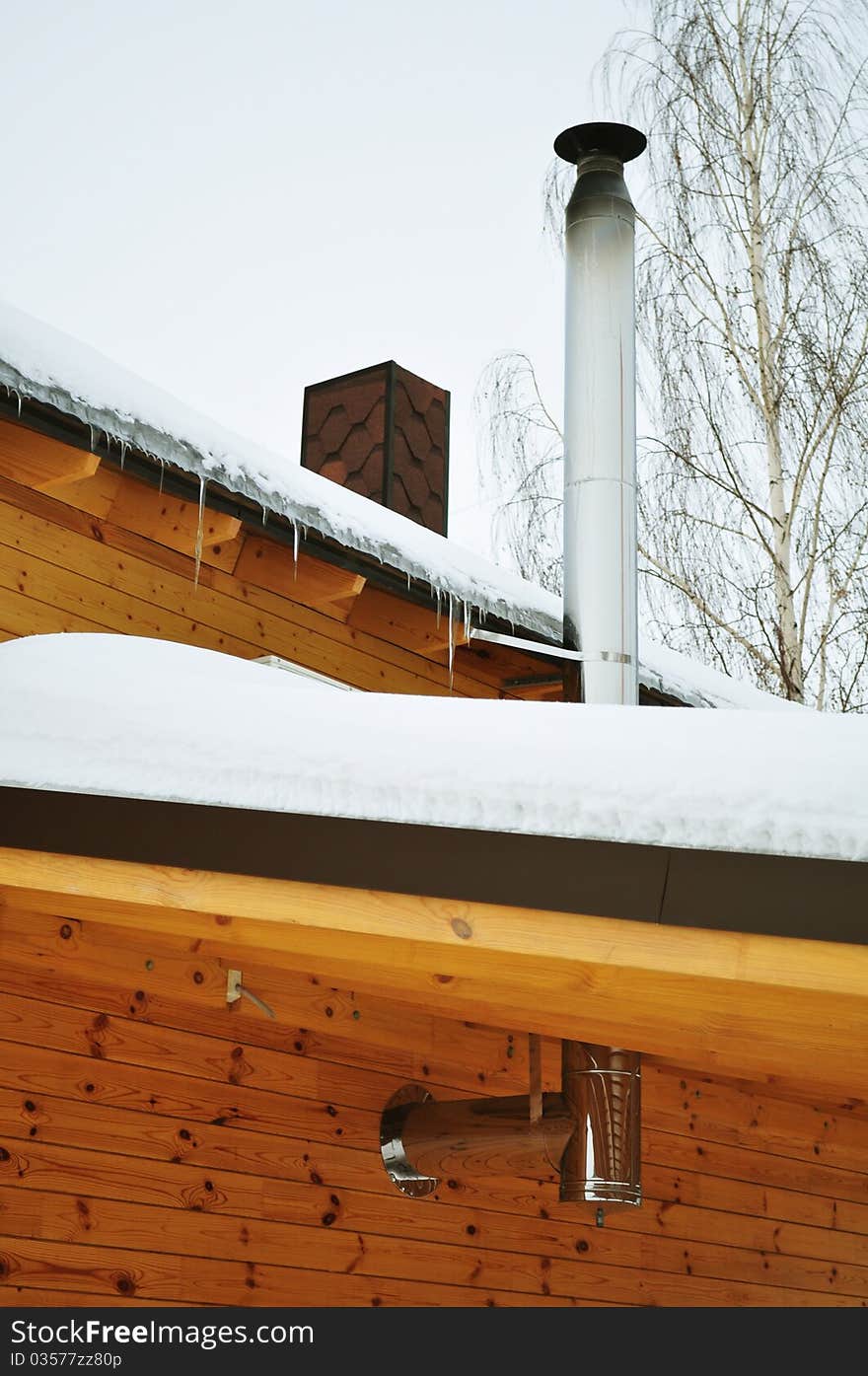 Suburban home, house with a tube, roof with icicles, metallic construction, cottage or chalet of stained wood, prefabricated buildings, winter trees, snow, white and brown. Suburban home, house with a tube, roof with icicles, metallic construction, cottage or chalet of stained wood, prefabricated buildings, winter trees, snow, white and brown