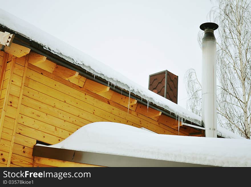 Suburban home, house with a pipe, roof with icicles, metallic construction, cottage or chalet of stained wood, prefabricated buildings, winter trees, snow, white and brown. Suburban home, house with a pipe, roof with icicles, metallic construction, cottage or chalet of stained wood, prefabricated buildings, winter trees, snow, white and brown