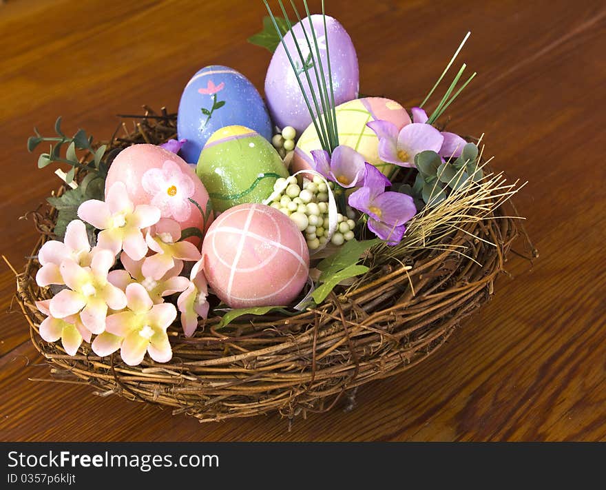 Painted Easter eggs in nest with flowers and side view on a wooden table