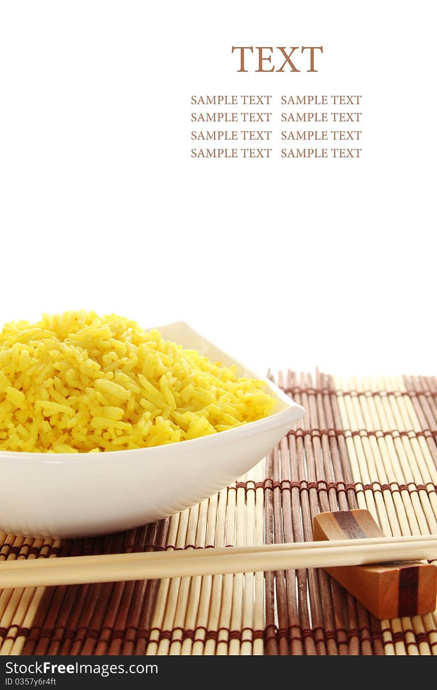 Boiled yellow rice and a white plate beside lie wooden sticks. Plate stands on a wooden mat. Isolated on a white background. Boiled yellow rice and a white plate beside lie wooden sticks. Plate stands on a wooden mat. Isolated on a white background