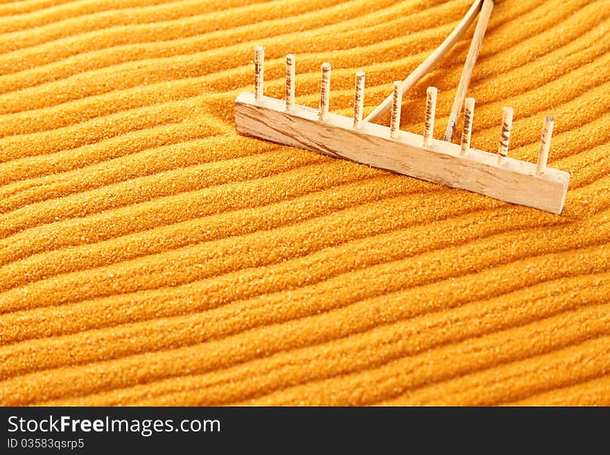 On the golden (orange) sand with wooden rakes made strips. Beside these wooden rakes. Rake in Zen Garden taken closeup