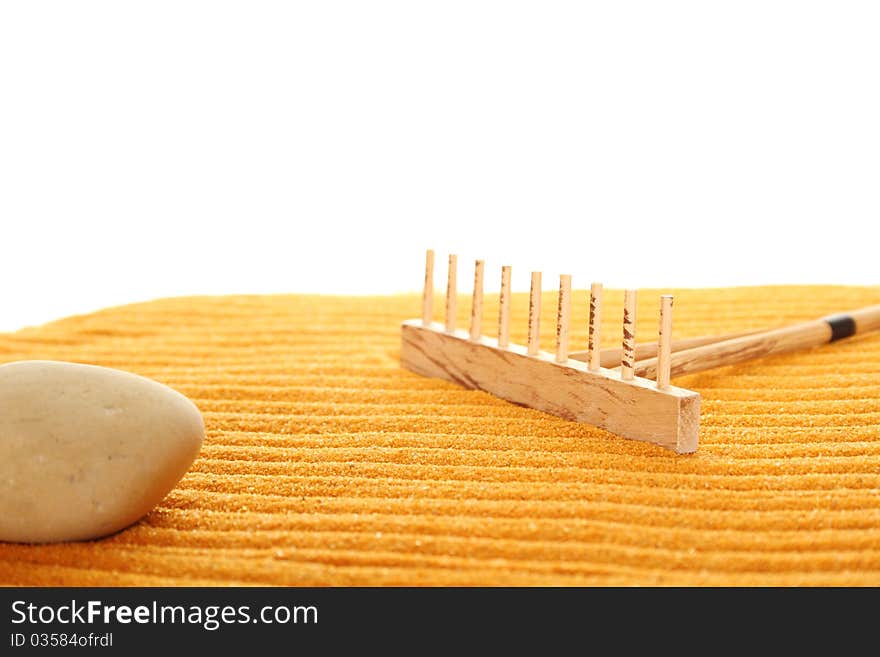 On the golden (orange) sand with wooden rakes made strips. Beside these wooden rakes. Rake in Zen Garden taken closeup