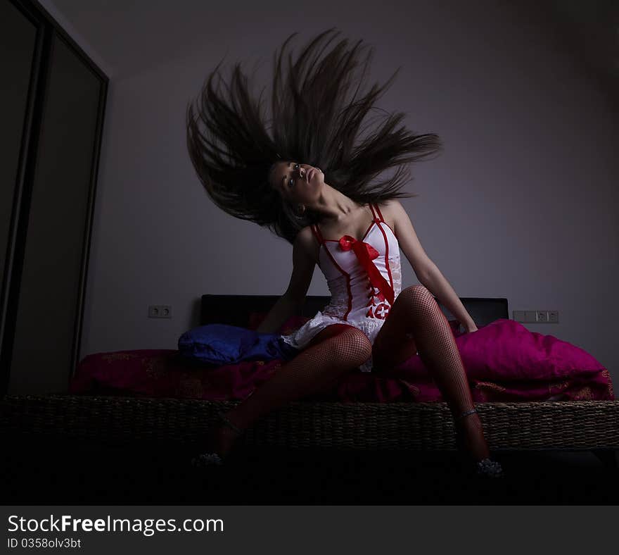 Girl sitting on the bed waving long hair. Photo.