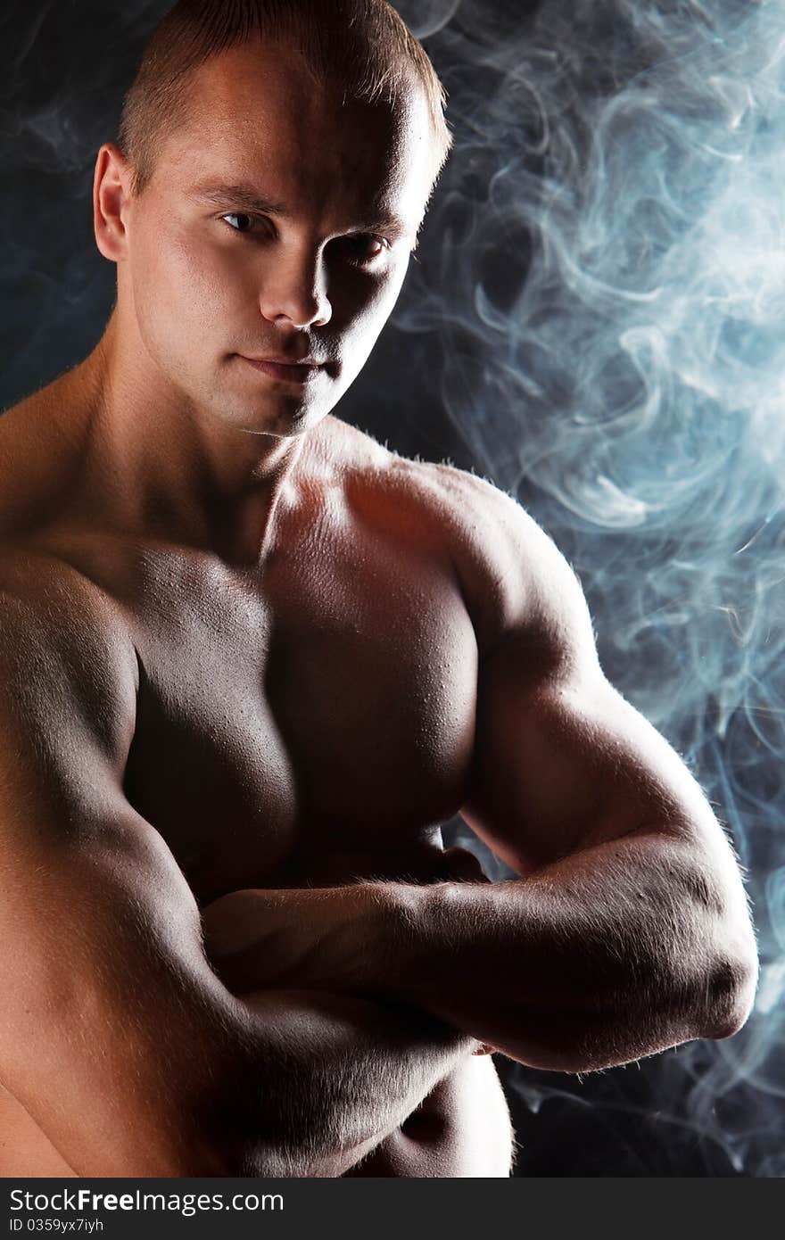 Young sporty man over Smoke. Muscles, a close up