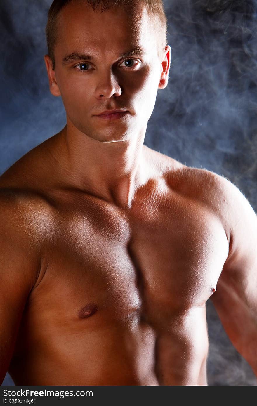 Young sporty man over Smoke. Muscles, a close up