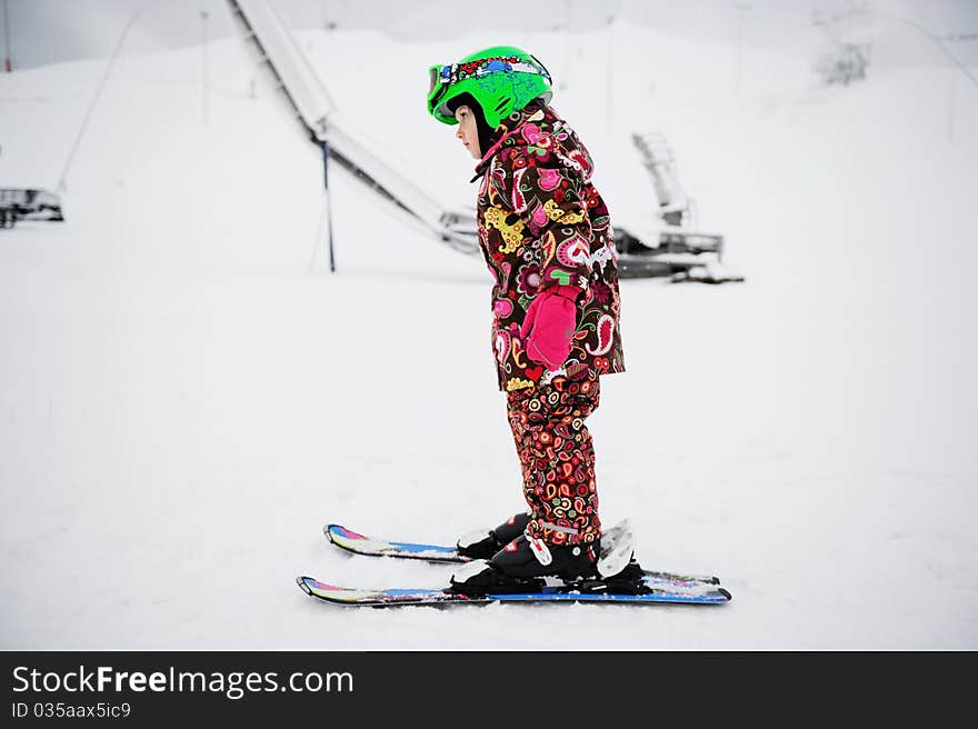 Little girl in colorful snowsuit and green helmet on Alpine ski. Little girl in colorful snowsuit and green helmet on Alpine ski