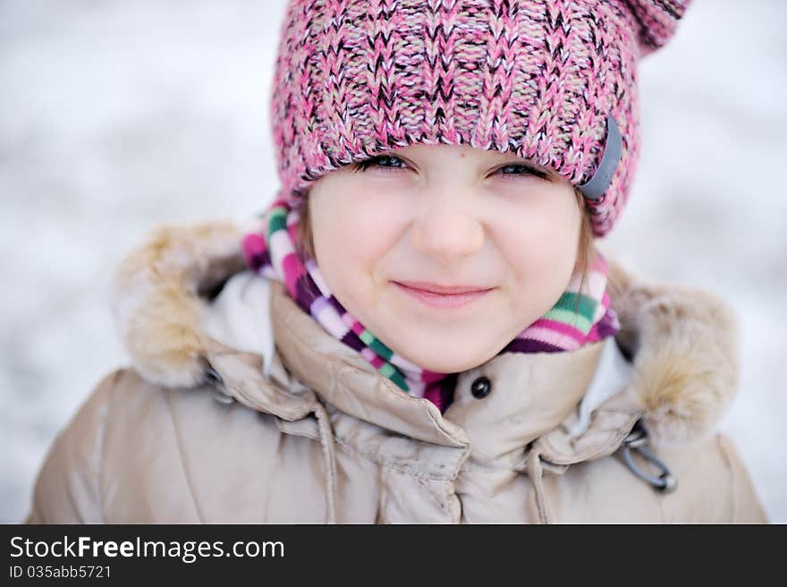 Winter portrait of adorable small girl with blue eyes in pink hat looks into the camera