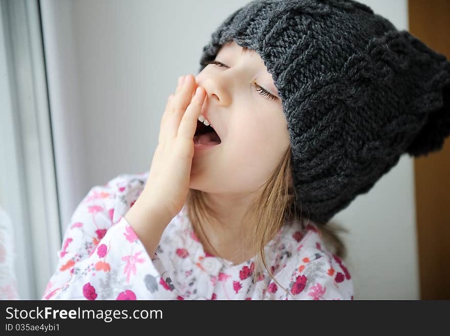 Adorable little kid girl with blue eyes in dark grey knit hat looks into the window. Adorable little kid girl with blue eyes in dark grey knit hat looks into the window