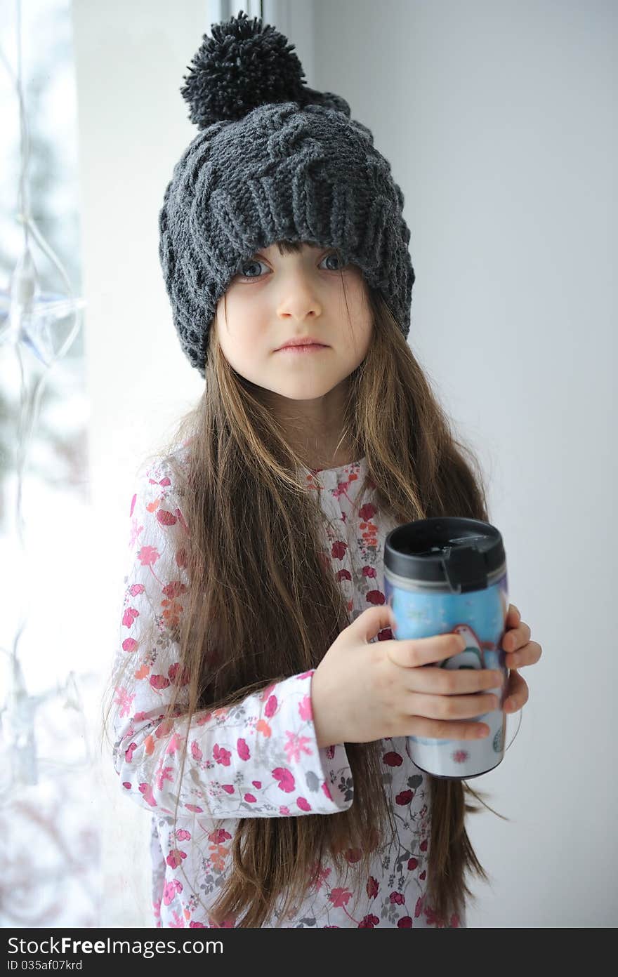 Adorable little kid girl with blue eyes in dark grey knit hat with cup. Adorable little kid girl with blue eyes in dark grey knit hat with cup