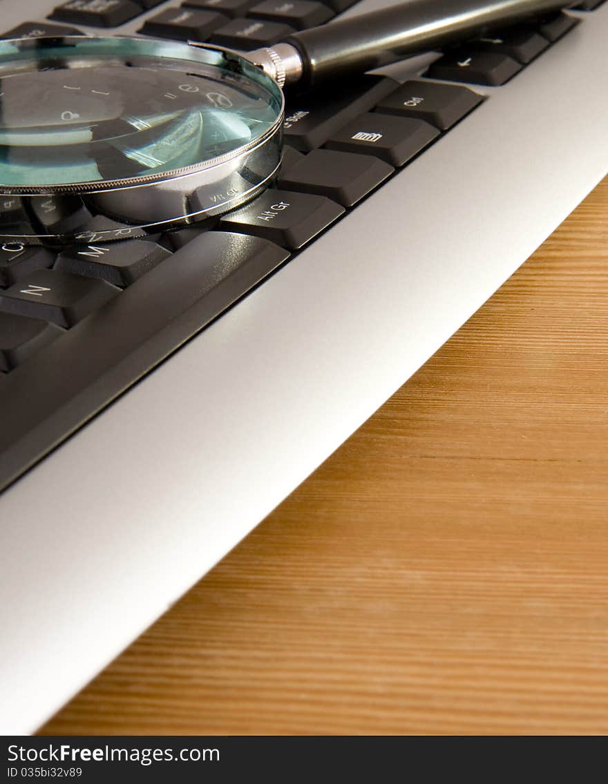 Computer keyboard and magnifying glass on wood table