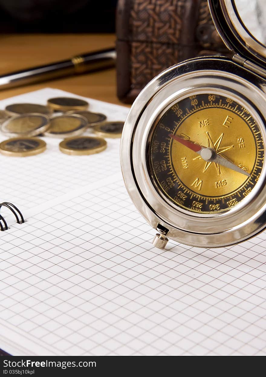 Compass, gold coin and pen on checked notebook. Compass, gold coin and pen on checked notebook