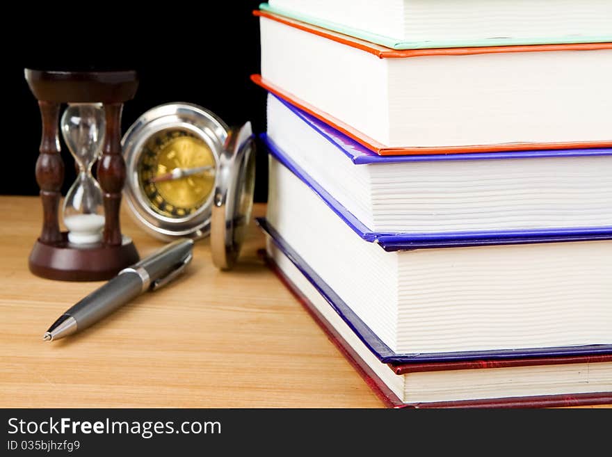 Pile of books, pen and hourglass on black background