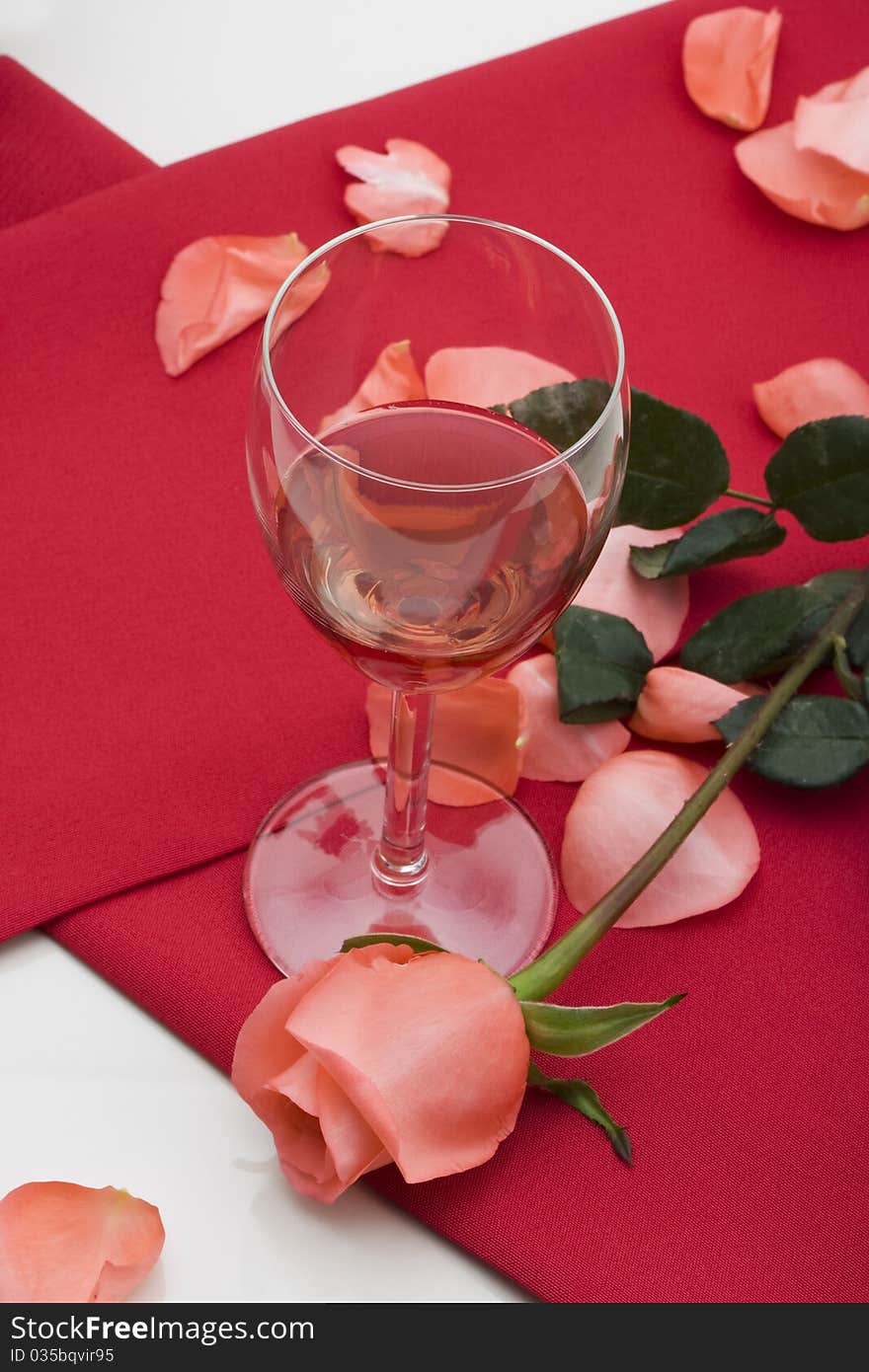 Glass of red wine with red table cloth and pink rose on on white background.