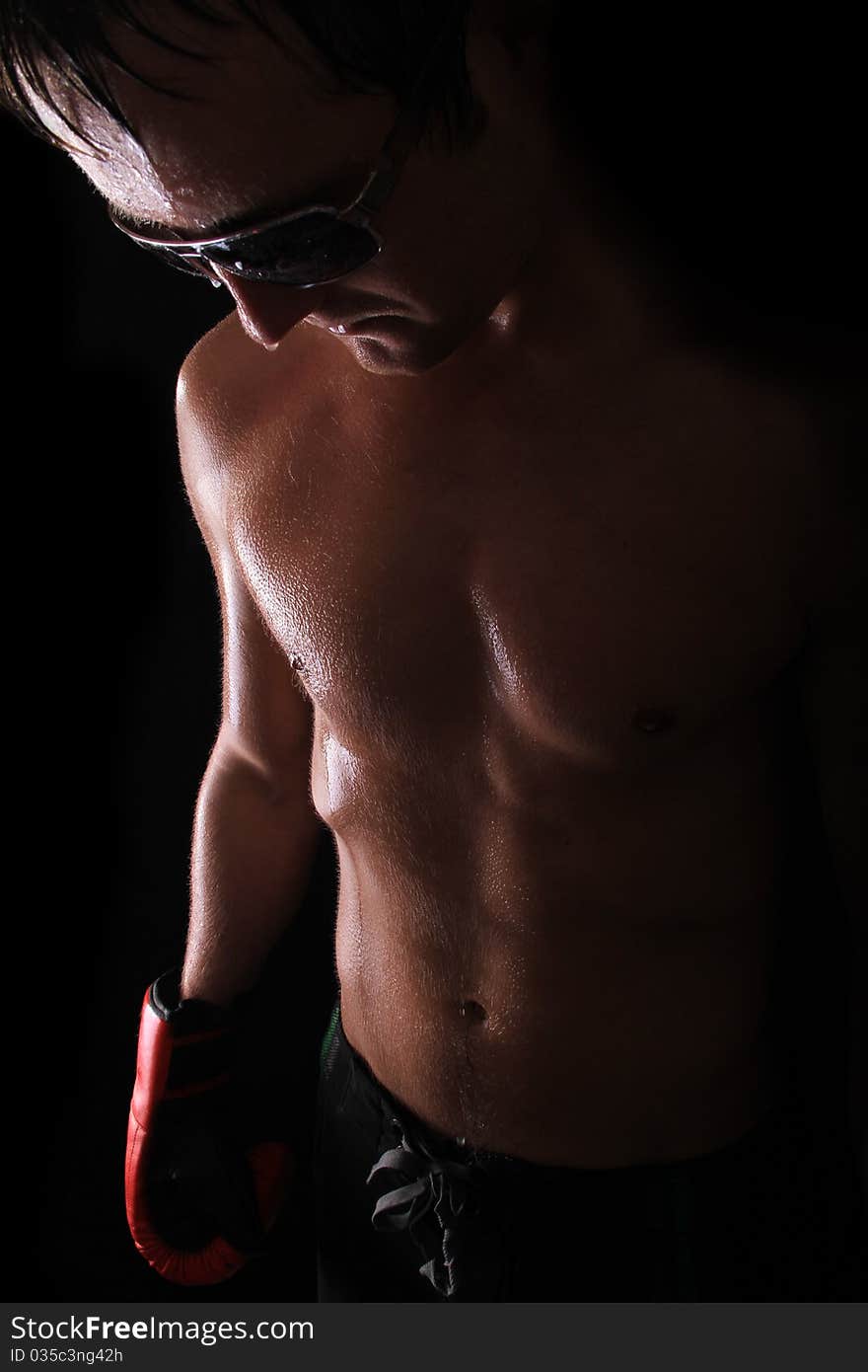 Sweated out model stands against a black background with boxing gloves on and shades. Sweated out model stands against a black background with boxing gloves on and shades