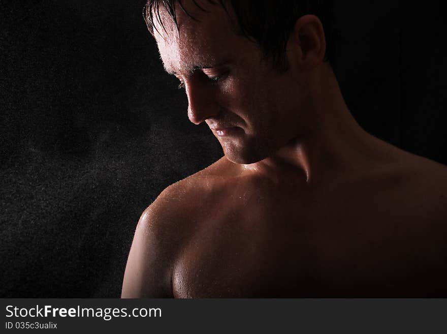 Male model standing against a black background with light shining in his face. water is also sprayed in the face of the model. Male model standing against a black background with light shining in his face. water is also sprayed in the face of the model