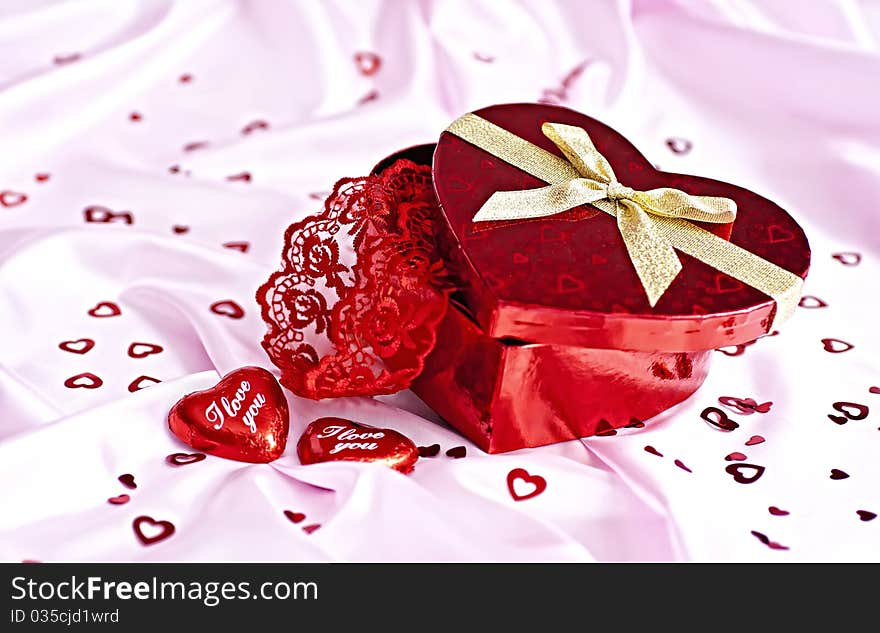 Pink bedding, gift box heart-shaped chocolate candy with the words I Love You and a lot of small distributed hearts. Surprise to the woman. Pink bedding, gift box heart-shaped chocolate candy with the words I Love You and a lot of small distributed hearts. Surprise to the woman.