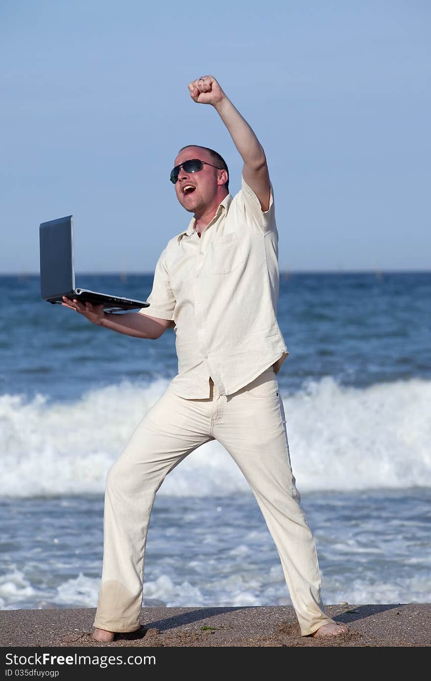 Young businessman at the beach with his laptop happy about success. Young businessman at the beach with his laptop happy about success