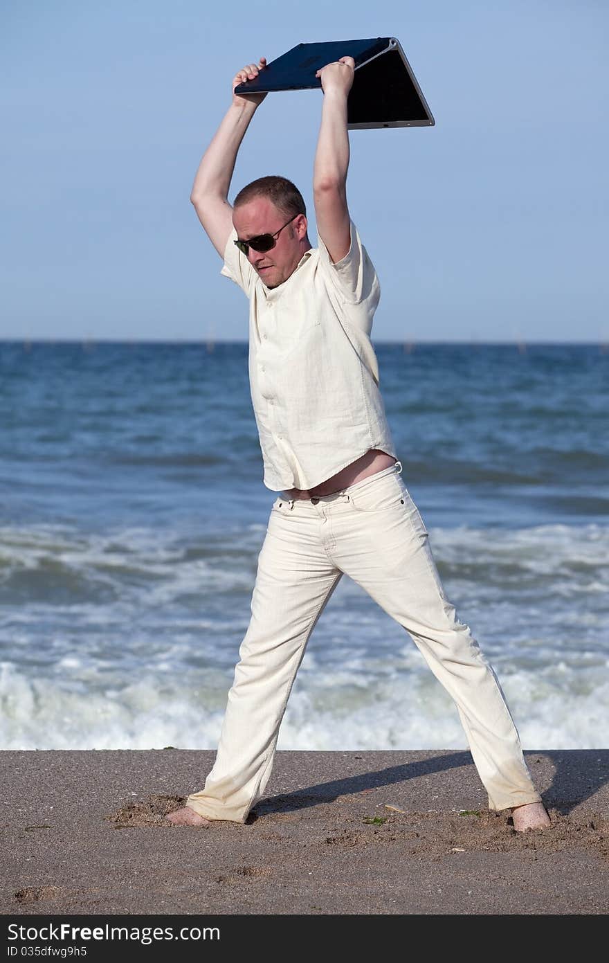 Sunburnt businessman at the beach throwing his laptop. Concept of protesting against work on vacation. Sunburnt businessman at the beach throwing his laptop. Concept of protesting against work on vacation