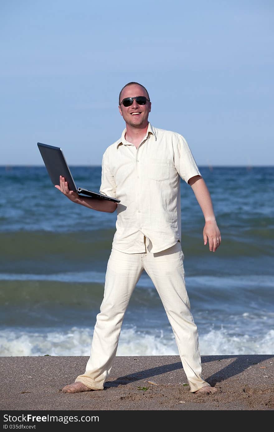 Young businessman at the beach with his laptop happy about success. Young businessman at the beach with his laptop happy about success